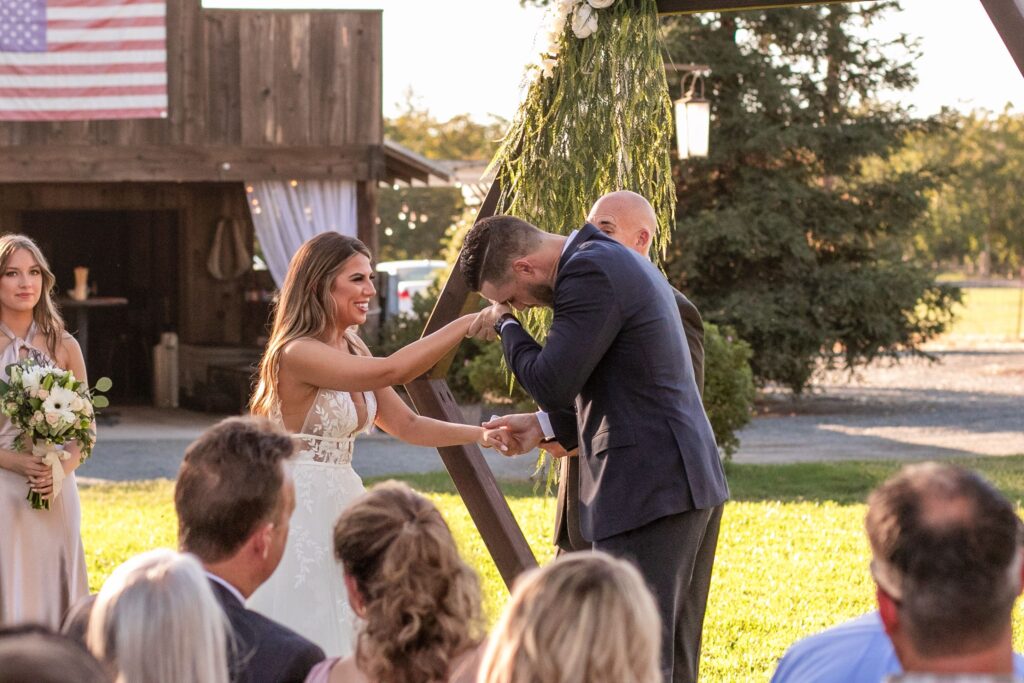Wedding ceremony with the bride and groom holding hands as the groom wipes tears from his face.