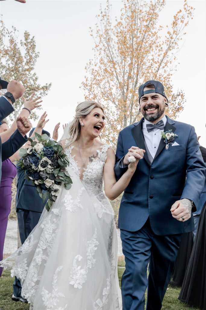 Bride and groom smiling while walking between people clapping and cheering for them.