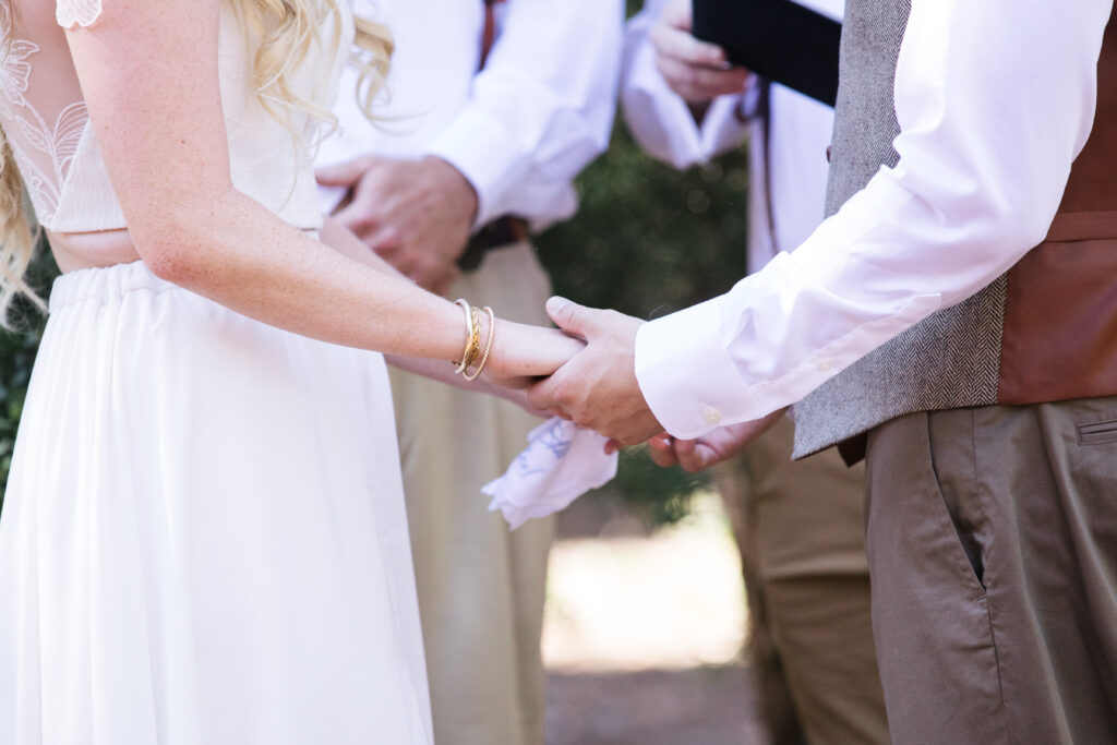 Woman in white and man in tan holding hands during a ceremony.