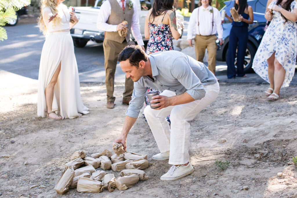 Man in a button-down shirt and white pants selecting a bag from the pile of filled brown paper bags.