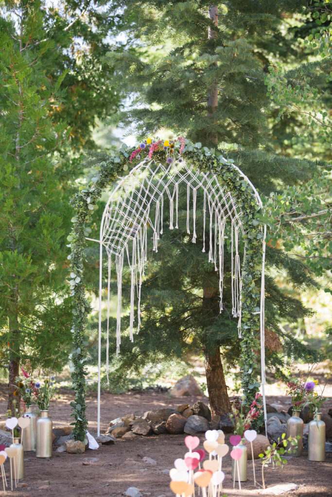 Wedding arch with macramé and flowers in a pine grove with wooden hearts down the aisle.