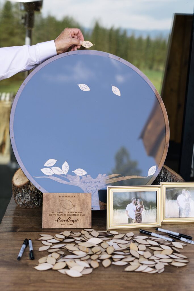 A round frame with an opening at the apex for small wood leaves to fall behind the glass, with a pile of small wood leaves set before it on a wood table.