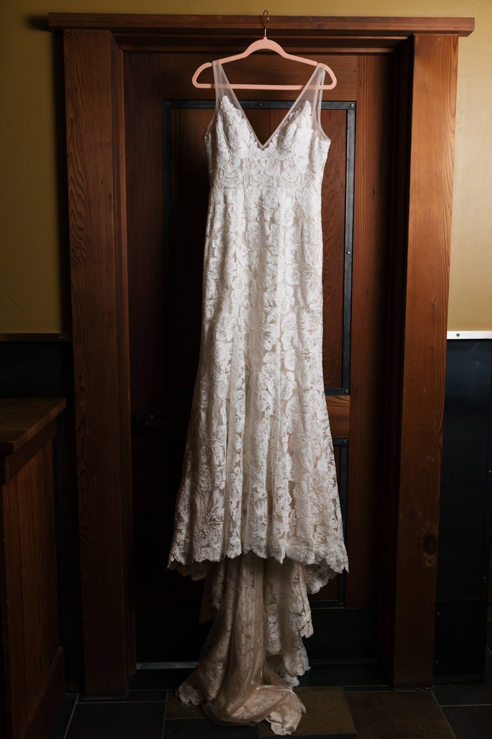 White lace wedding dress hanging in front of a wood door.