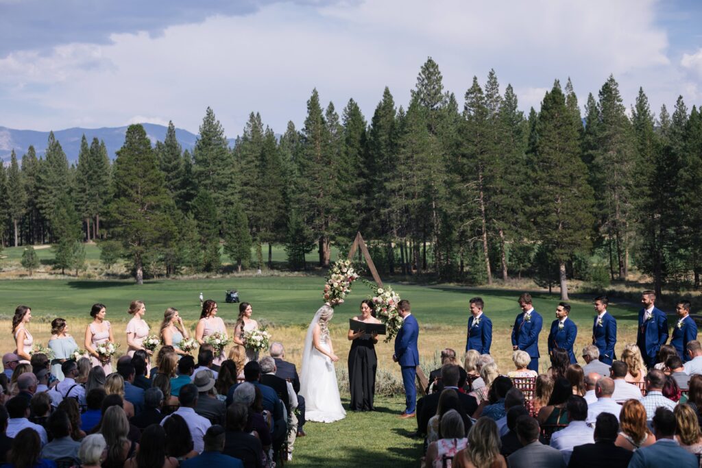 Wedding ceremony with a golf course and pine tree backdrop.