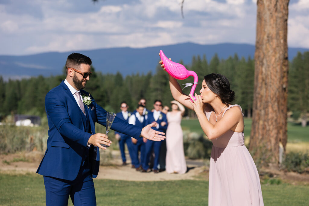 A man in a blue suit cheers on a woman in a pink dress drinking out of a pink flamingo.