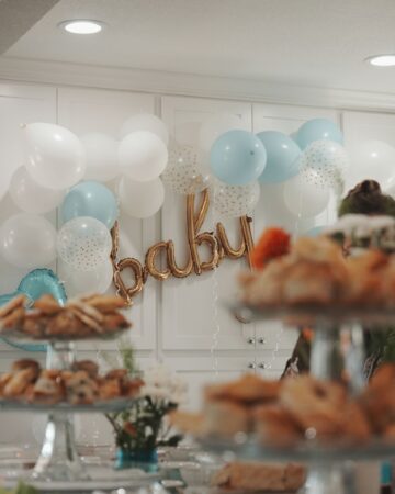 Out of focus crystal tiers of baked goods in the foreground with blue and white balloons decorating white cabinets in the background in focus.