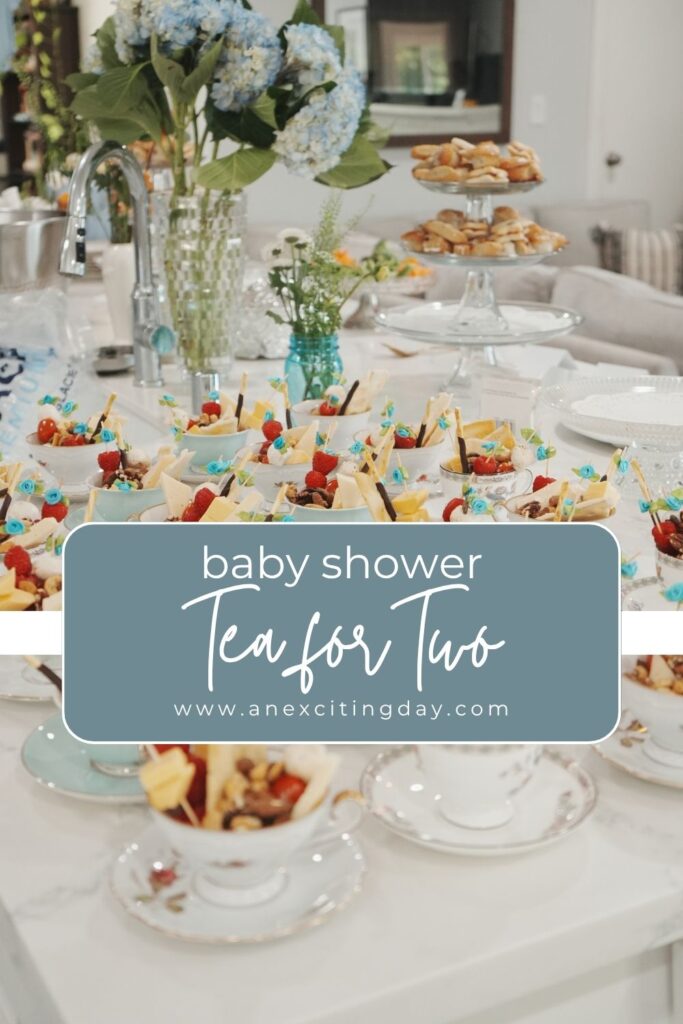 White marble tabletop with teacups filled with cheese and crackers, all with overlay text reading "baby shower Tea for Two".