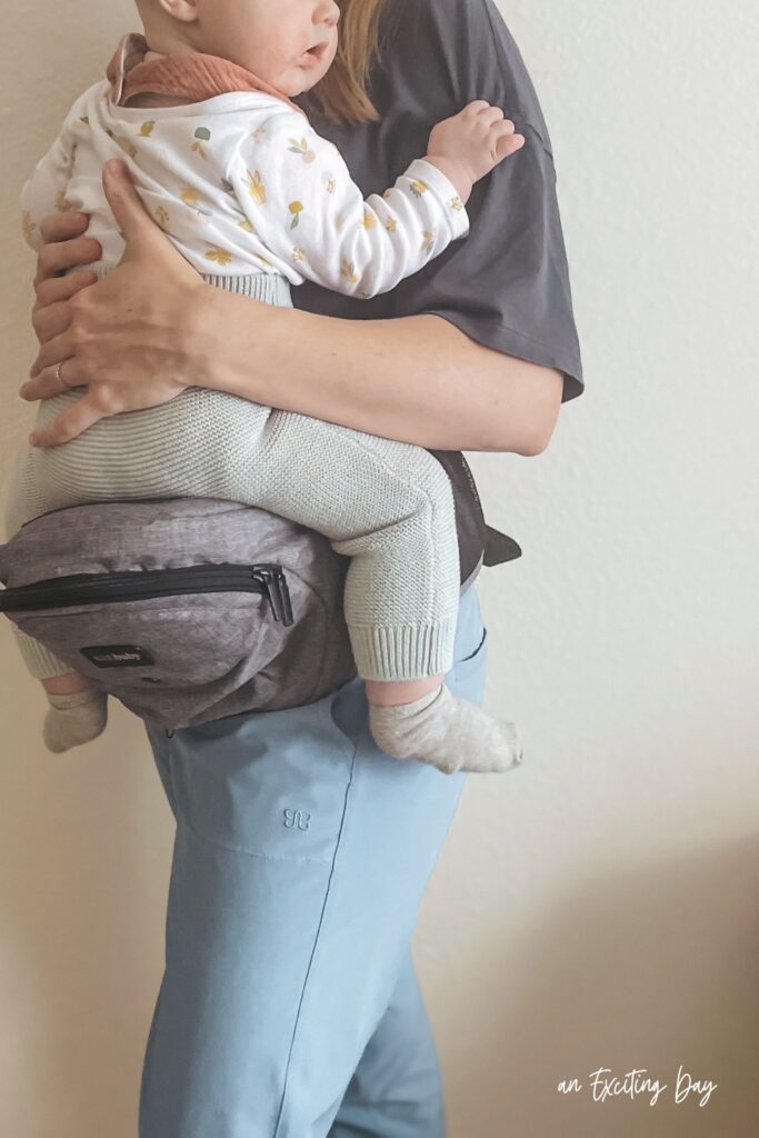 Baby seated atop a hip carrier facing a woman holding them.