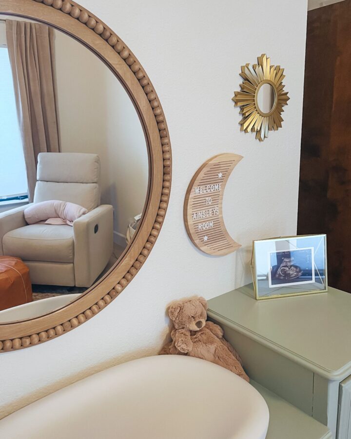 Baby changing station atop a green dresser with a wooden framed mirror on the wall above the changing pad.