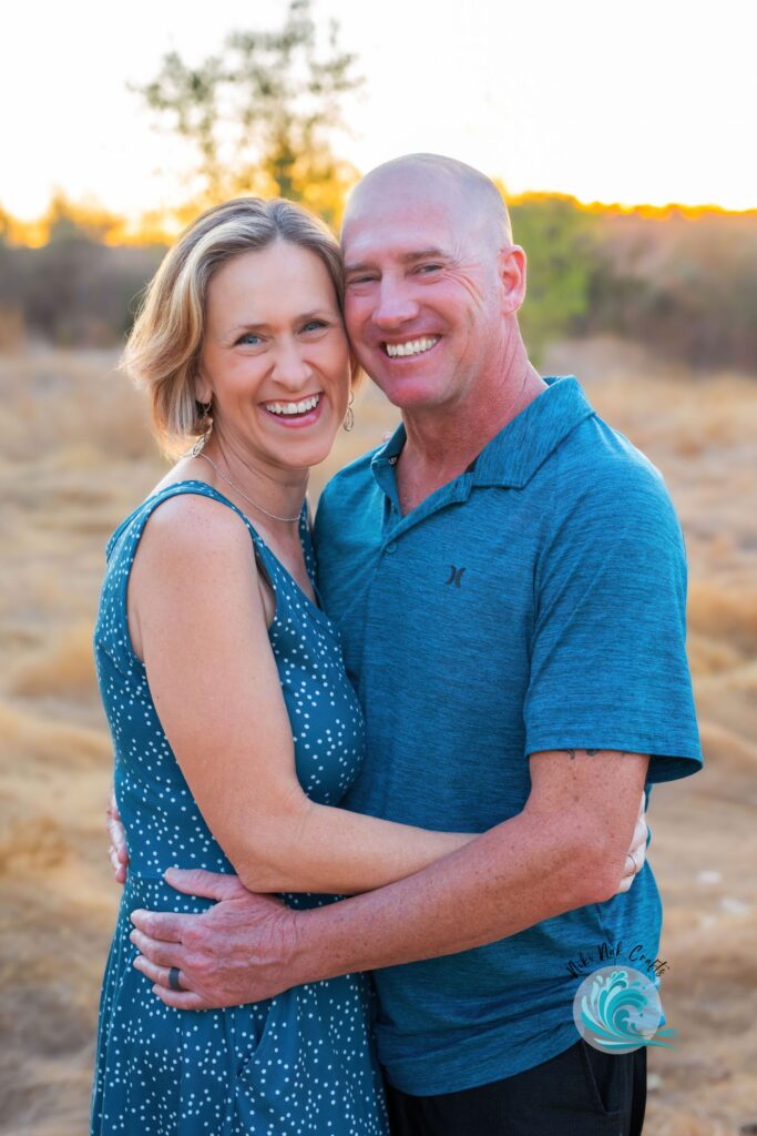 One woman and one man smiling in an embrace outside at golden hour, both wearing shades of blue.