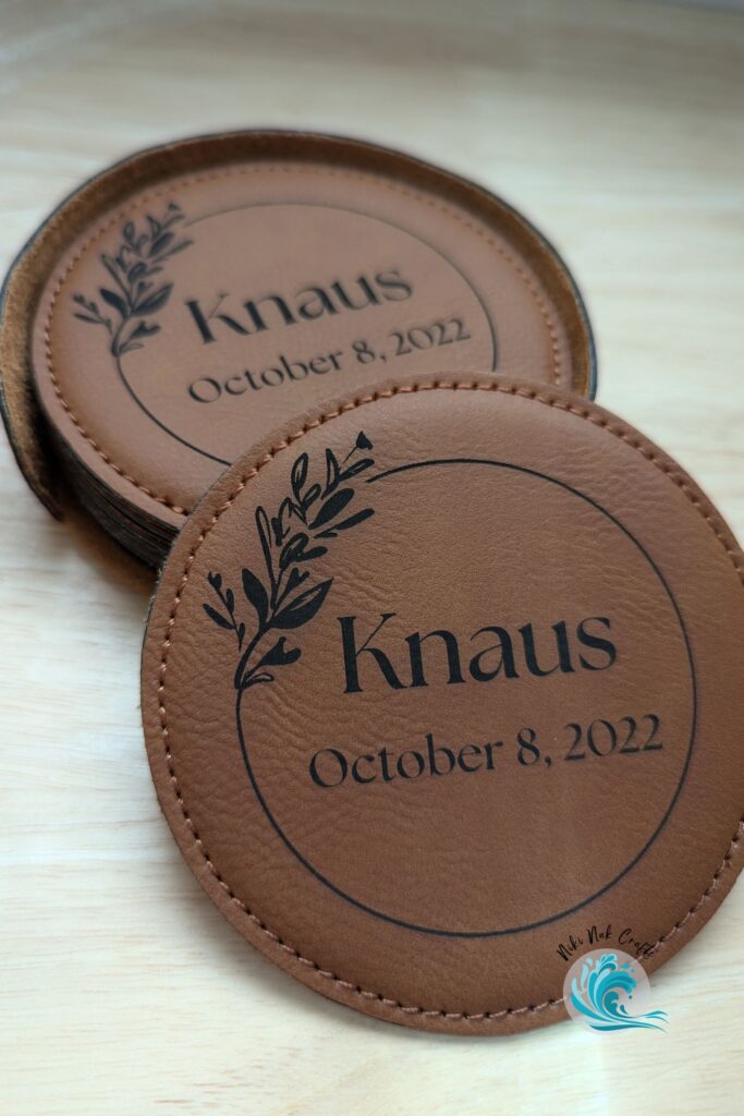 Leather coasters printed with "Knaus October 8, 2022" with one situated in front of a stack of others.