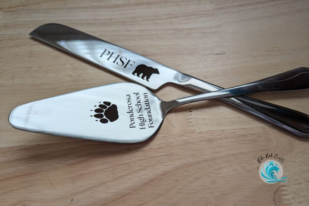 Silver metal cake cutting knife and server set printed with "Ponderosa High School Foundation" with a bear paw print on the server, and "PHSF" with a bear silhouette on the knife.