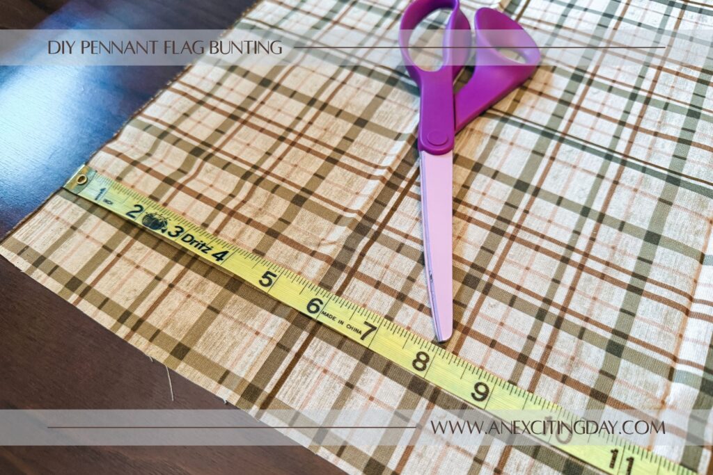 Sewing project scene with tan plaid fabric spread atop a desk with a measuring tape across the fabric and fabric shears pointing at "8 inches" on the measuring tape. Overlay text reads "diy pennant flag bunting: and "www.anexcitingday.com".