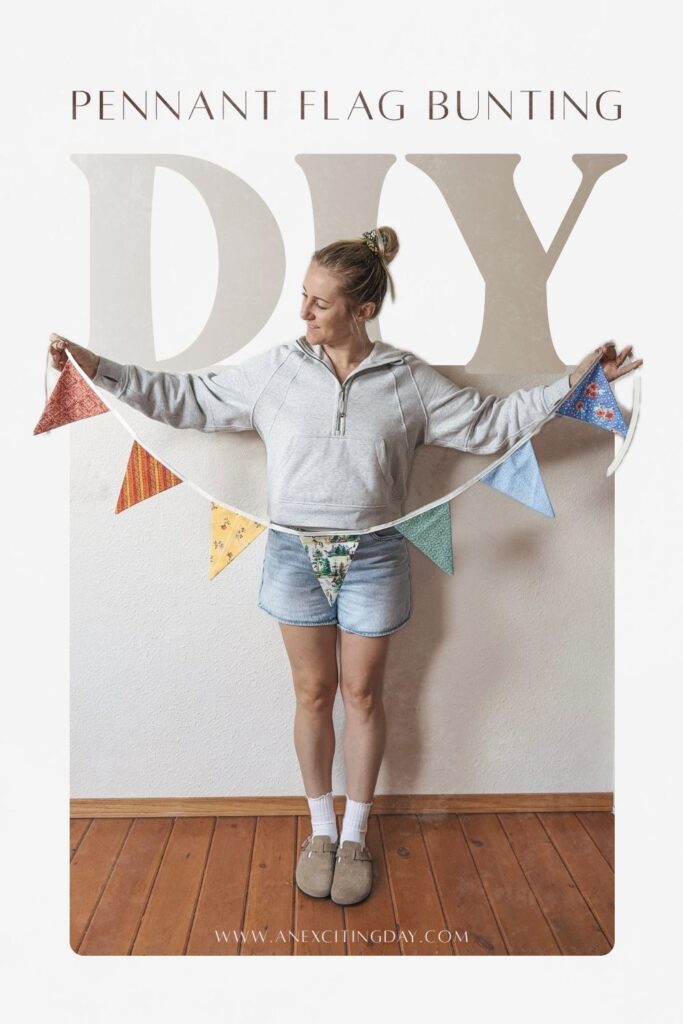 Woman in grey suede clogs, a grey hooded sweatshirt and light wash denim shorts holding a colorful pennant flag bunting in front of her. Overlay text reading "pennant flag bunting DIY" and "www.anexcitingday.com".