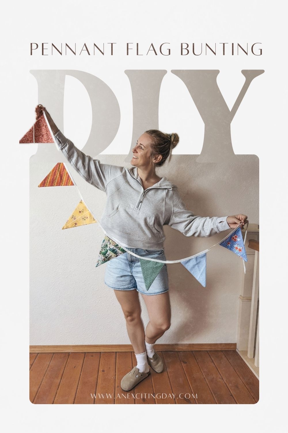 Woman in grey suede clogs, a grey hooded sweatshirt and light wash denim shorts holding a colorful pennant flag bunting. Overlay text reading "pennant flag bunting DIY" and "www.anexcitingday.com".